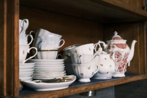 A wooden shelf filled with a collection of vintage teapots and stacked teacups, illustrating the value of antique china as a tangible collectible asset